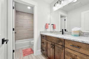 Full bathroom with vanity, toilet, tiled shower / bath, and hardwood / wood-style floors