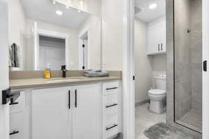 Bathroom with vanity, a tile shower, toilet, and tile patterned floors