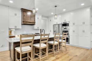 Kitchen featuring appliances with stainless steel finishes, an island with sink, pendant lighting, and white cabinets