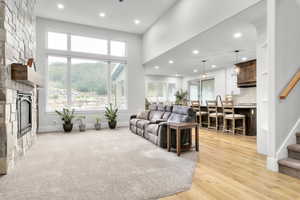 Living room with a stone fireplace, light hardwood / wood-style flooring, a high ceiling, and a wealth of natural light