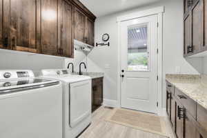 Clothes washing area featuring cabinets, sink, washer and clothes dryer, and light hardwood / wood-style floors