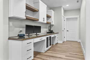 Office or work station featuring built in desk, light hardwood / wood-style flooring, and white cabinets