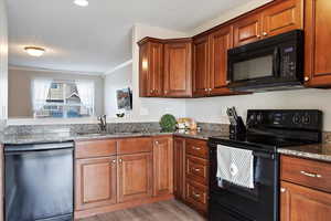 Kitchen featuring granite countertops, LVP flooring, black appliances and large sliding glass door with painted deck.