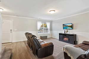 Family room with crown moulding, wainscoting trim, carpet and laminate in traffic areas, wall mounted TV.