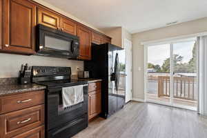 Kitchen featuring granite countertops, LVP flooring, black appliances and large sliding glass door with painted deck.