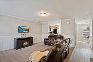 Family room with crown moulding, wainscoting trim, carpet and laminate in traffic areas, wall mounted TV.