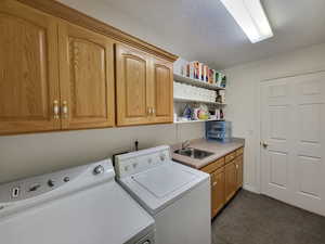 Laundry room featuring sink, a textured ceiling, washer and clothes dryer, dark carpet, and cabinets