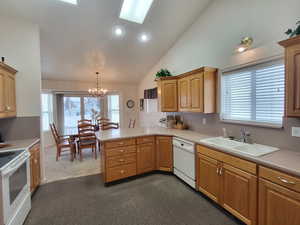 Kitchen featuring lofted ceiling, dark carpet, kitchen peninsula, decorative light fixtures, and white appliances