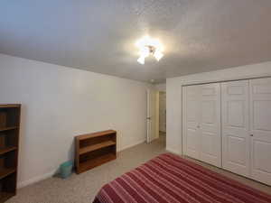 Unfurnished bedroom featuring a textured ceiling, a closet, and light colored carpet