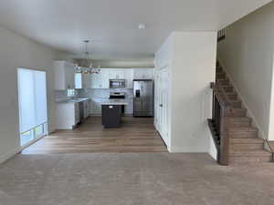 Kitchen featuring white cabinetry, appliances with stainless steel finishes, a center island, and decorative light fixtures