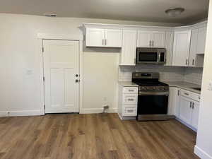 Kitchen with decorative backsplash, white cabinetry, stainless steel appliances, and dark hardwood / wood-style floors