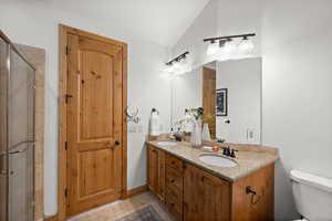 Bathroom featuring lofted ceiling, tile patterned flooring, vanity, an enclosed shower, and toilet