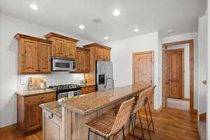 Kitchen with tasteful backsplash, a breakfast bar area, light stone counters, stainless steel appliances, and a center island with sink