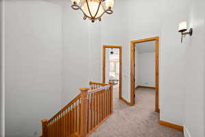 Hallway featuring light carpet and an inviting chandelier