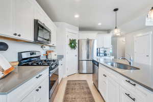 Kitchen featuring sink, light wood-type flooring, white cabinetry, stainless steel appliances, and pendant lighting