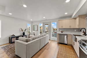 Kitchen with stainless steel appliances, backsplash, light wood-type flooring, light brown cabinetry, and sink