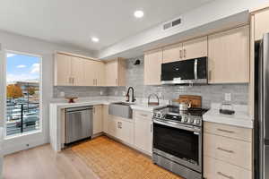 Kitchen with stainless steel appliances, tasteful backsplash, light brown cabinetry, light hardwood / wood-style flooring, and sink