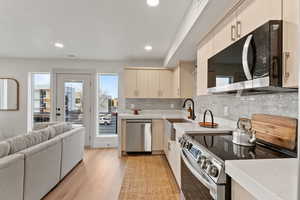 Kitchen with backsplash, sink, cream cabinetry, light hardwood / wood-style floors, and stainless steel appliances