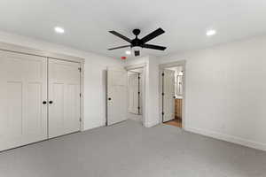 Unfurnished bedroom with ensuite bath, ceiling fan, a closet, and light colored carpet