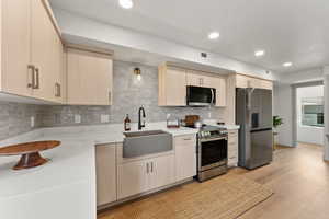 Kitchen featuring sink, tasteful backsplash, light wood-type flooring, light brown cabinetry, and appliances with stainless steel finishes