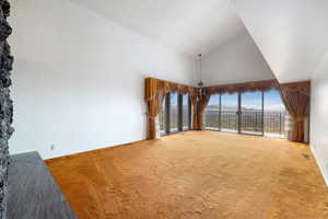 Unfurnished living room featuring carpet flooring, vaulted ceiling, and plenty of natural light