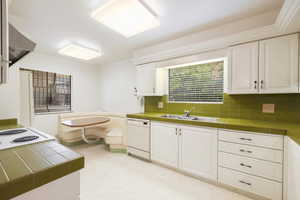 Kitchen featuring tile counters, backsplash, white dishwasher, sink, and white cabinets