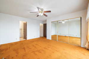 Unfurnished bedroom featuring a textured ceiling, ensuite bathroom, light colored carpet, and ceiling fan