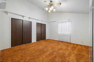 Unfurnished bedroom featuring a textured ceiling, multiple closets, carpet floors, ceiling fan, and lofted ceiling