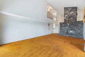 Unfurnished living room with a stone fireplace, carpet flooring, and a towering ceiling