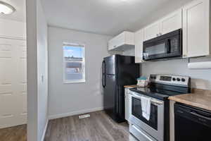 Kitchen with laminate wood-style floors, black appliances, and white cabinetry