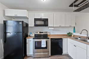 Kitchen featuring white cabinets, laminate wood-style floors, black appliances, and sink