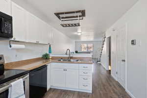 Kitchen with kitchen peninsula, black appliances, laminate wood-style flooring, white cabinetry, and sink