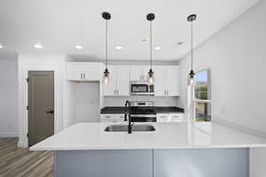 Kitchen featuring appliances with stainless steel finishes, sink, light wood-type flooring, and pendant lighting