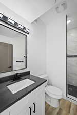 Bathroom with toilet, hardwood / wood-style floors, vanity, a tile shower, and a textured ceiling