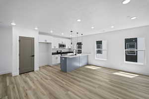 Kitchen featuring a center island with sink, white cabinets, pendant lighting, light wood-type flooring, and appliances with stainless steel finishes