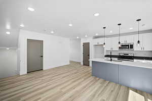 Kitchen with sink, white cabinets, pendant lighting, light wood-type flooring, and appliances with stainless steel finishes