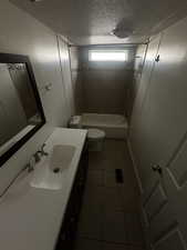 Full bathroom featuring toilet, tile patterned flooring, tiled shower / bath, vanity, and a textured ceiling