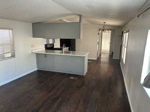 Kitchen featuring sink, vaulted ceiling, dark hardwood / wood-style flooring, kitchen peninsula, and a chandelier