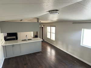 Kitchen featuring kitchen peninsula, vaulted ceiling, dark wood-type flooring, sink, and a chandelier