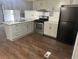 Kitchen featuring kitchen peninsula, gas range, dark wood-type flooring, black refrigerator, and sink