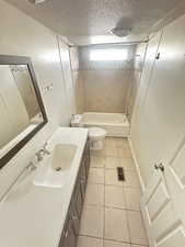 Full bathroom featuring a textured ceiling, toilet, tile patterned floors, tiled shower / bath, and vanity