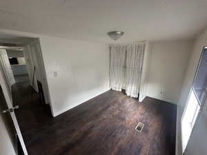 Empty room with a textured ceiling and dark hardwood / wood-style flooring