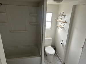 Bathroom with bathtub / shower combination, a textured ceiling, and toilet