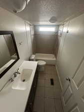 Full bathroom featuring a textured ceiling, toilet, tile patterned floors, tiled shower / bath, and vanity