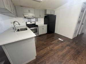 Kitchen with sink, kitchen peninsula, black fridge, dark wood-type flooring, and gas range