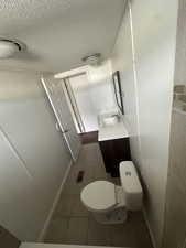 Bathroom with vanity, a textured ceiling, toilet, and tile patterned flooring