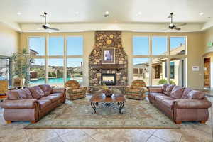 Tiled living room featuring ceiling fan, a stone fireplace, and a towering ceiling