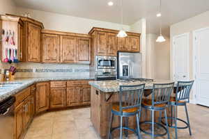 Kitchen featuring a kitchen island, stainless steel appliances, decorative light fixtures, light stone counters, and decorative backsplash