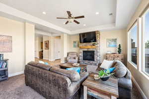 Carpeted living room featuring a raised ceiling, a fireplace, and ceiling fan