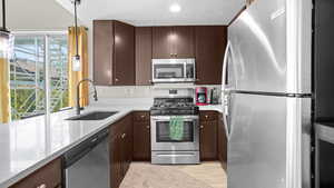 Kitchen featuring appliances with stainless steel finishes, a textured ceiling, light hardwood / wood-style flooring, sink, and decorative light fixtures